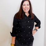 Woman wearing a black button-up shirt with white buttons against a plain background