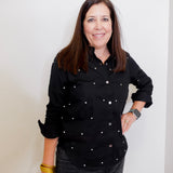 Woman wearing a black button-up shirt with white buttons against a plain background