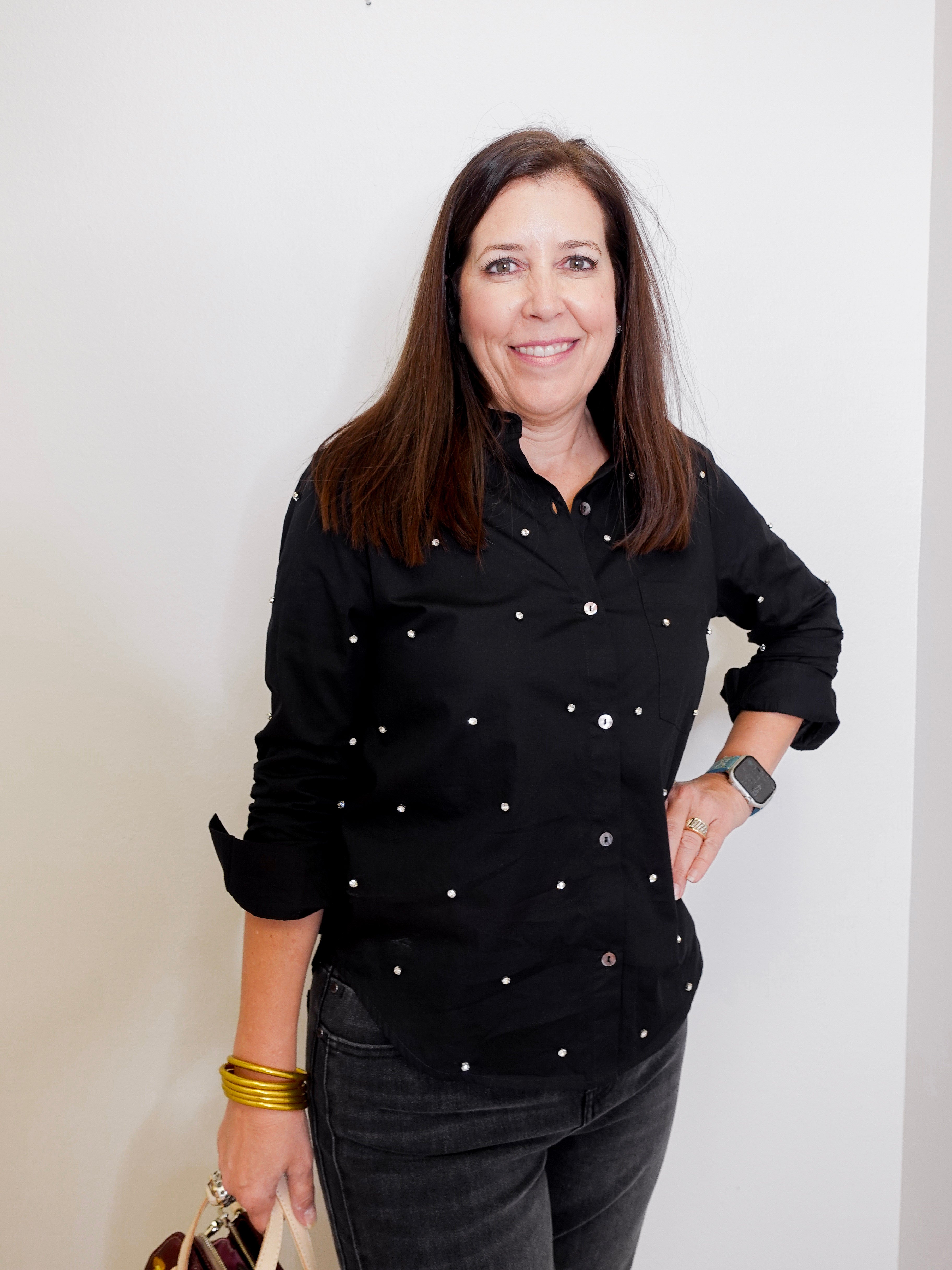 Woman wearing a black button-up shirt with white buttons against a plain background