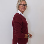 Person wearing a burgundy sweater over a white shirt against a plain background