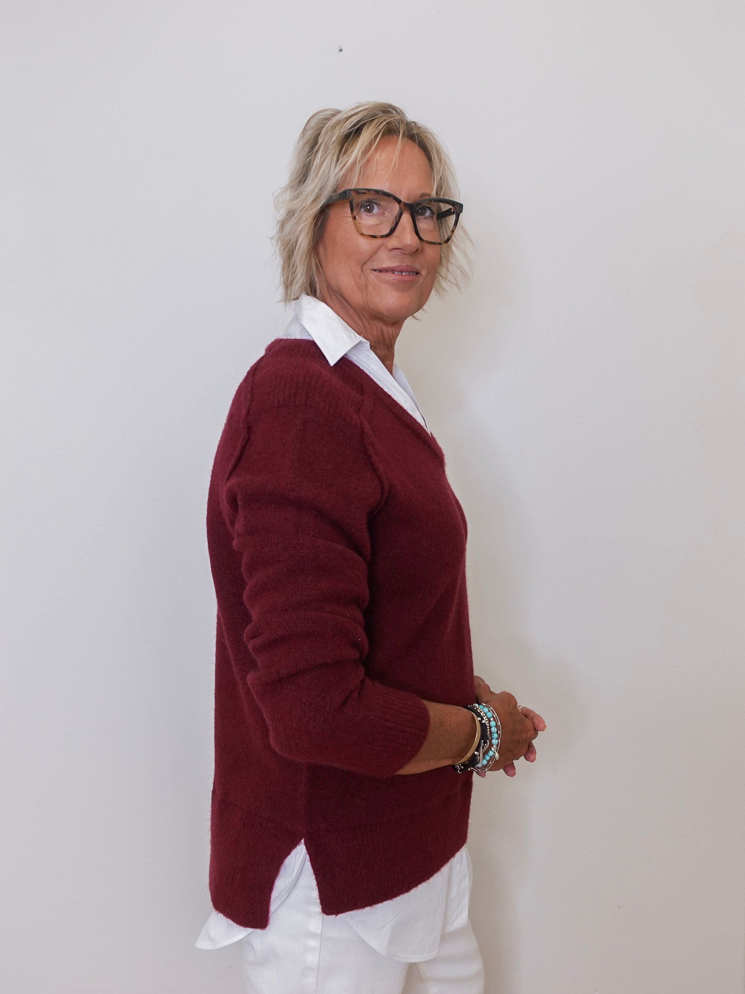 Person wearing a burgundy sweater over a white shirt against a plain background
