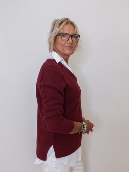 Person wearing a burgundy sweater over a white shirt against a plain background