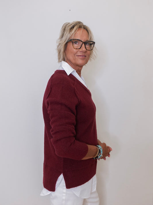 Person wearing a burgundy sweater over a white shirt against a plain background