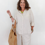Woman in beige outfit holding a woven bag against a white background