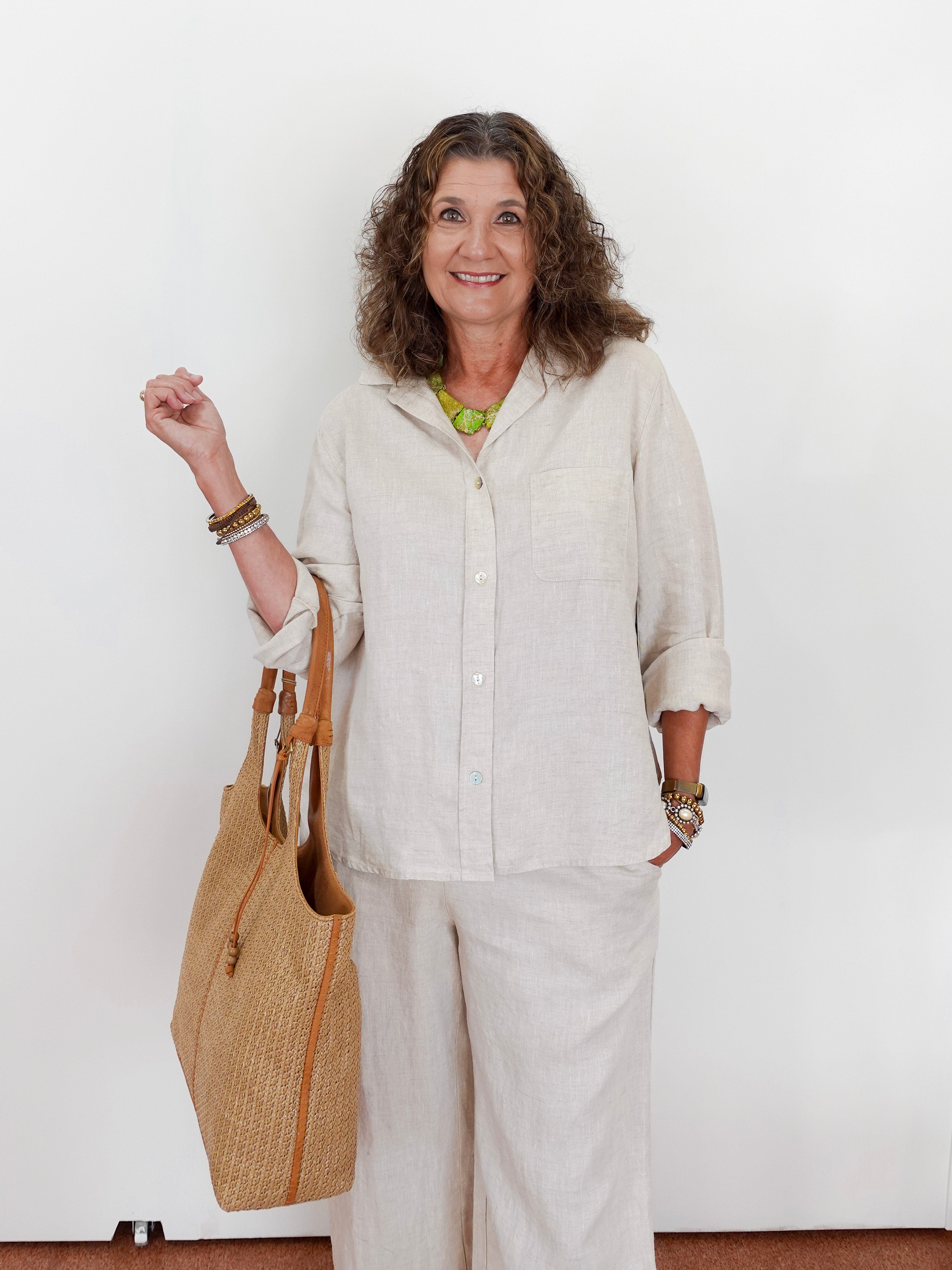 Woman in beige outfit holding a woven bag against a white background