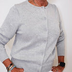 Person wearing a gray cardigan with pearl embellishments against a white background