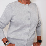 Person wearing a gray cardigan with pearl embellishments against a white background