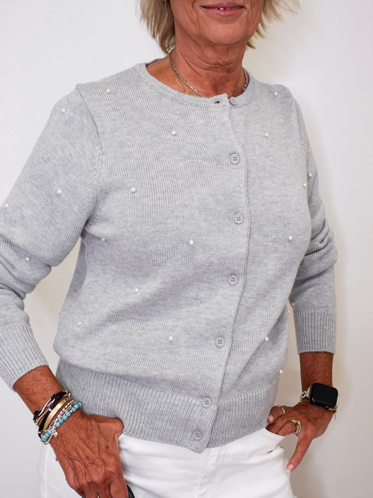 Person wearing a gray cardigan with pearl embellishments against a white background