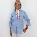 Woman wearing a light blue shirt and white pants against a white background
