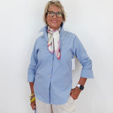Woman wearing a light blue shirt and white pants against a white background