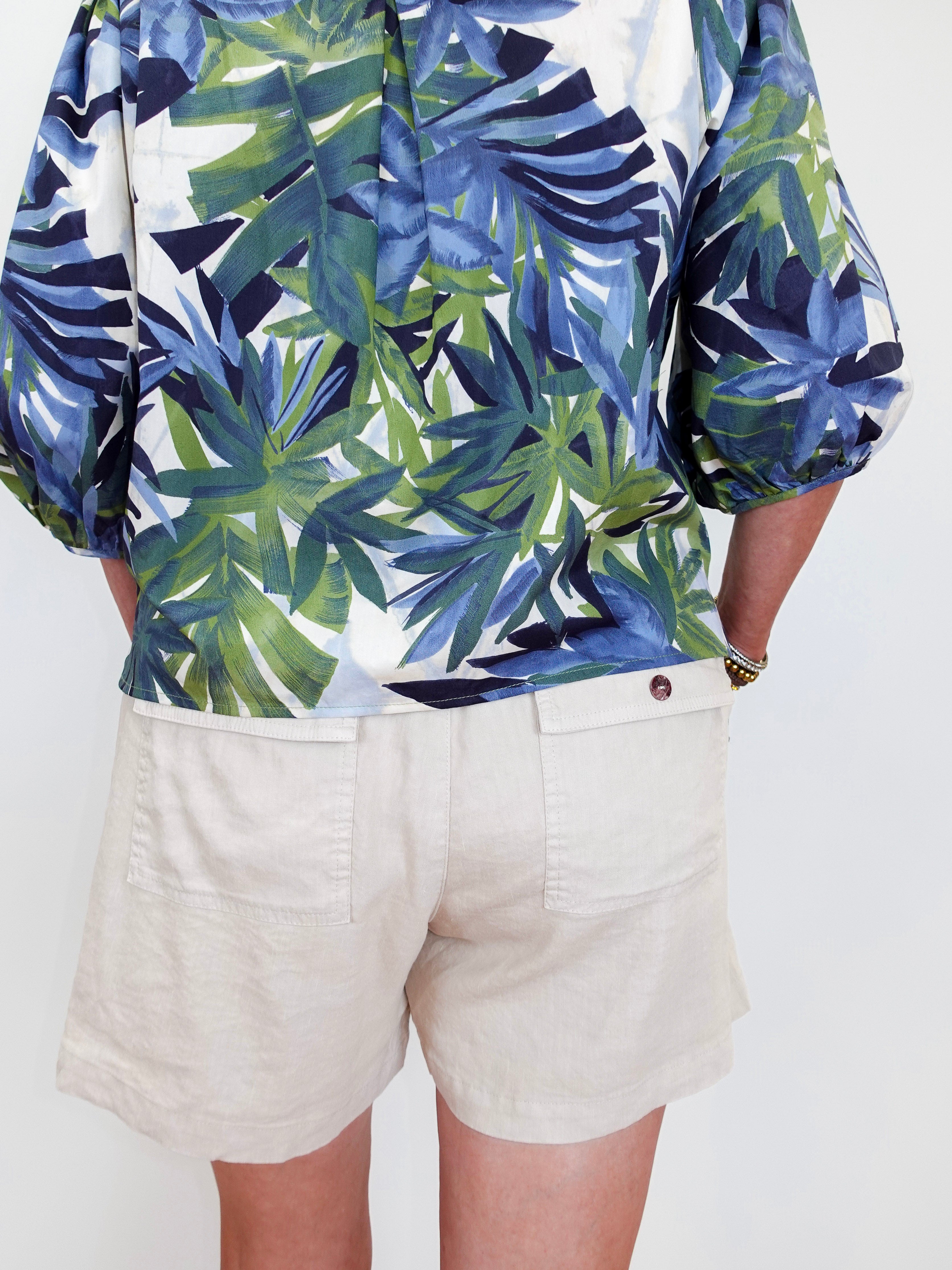 Person wearing a tropical leaf pattern shirt and beige shorts on a white background