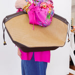 Person holding a large straw bag with a colorful jacket and blue pants.