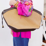 Person holding a large straw bag with a colorful jacket and blue pants.