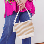 Person holding a woven handbag with a colorful top and blue jeans.