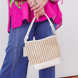 Person holding a woven handbag with a colorful top and blue jeans.