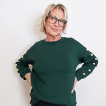 Woman wearing a green sweater with white buttons on a plain background