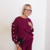 Woman wearing a burgundy outfit with pearl details against a white background