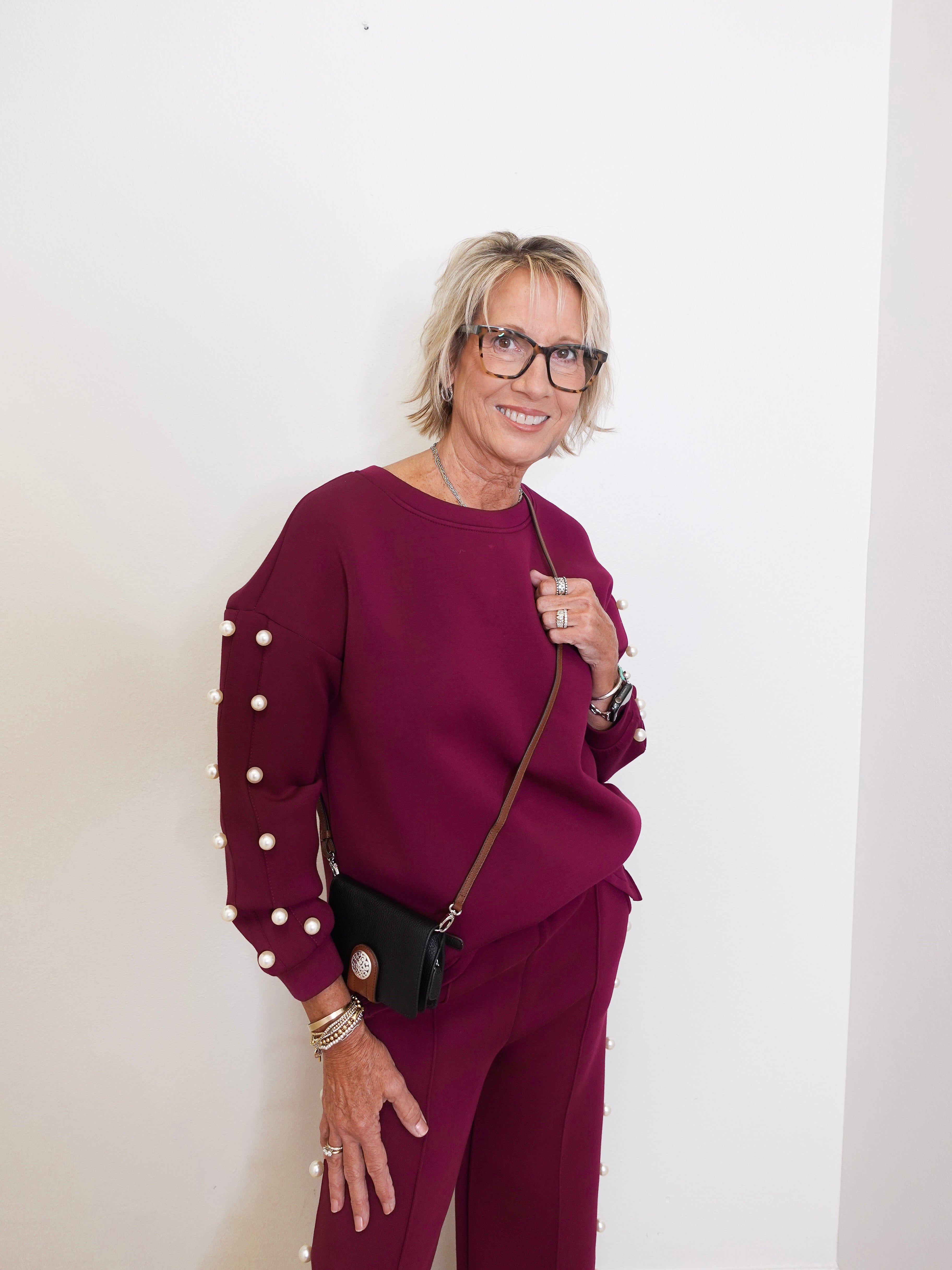 Woman wearing a burgundy outfit with pearl details against a white background