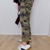 Person wearing camouflage pants and white sneakers on a wooden floor.