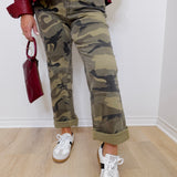 Person wearing camouflage pants and white sneakers, holding a red handbag indoors.