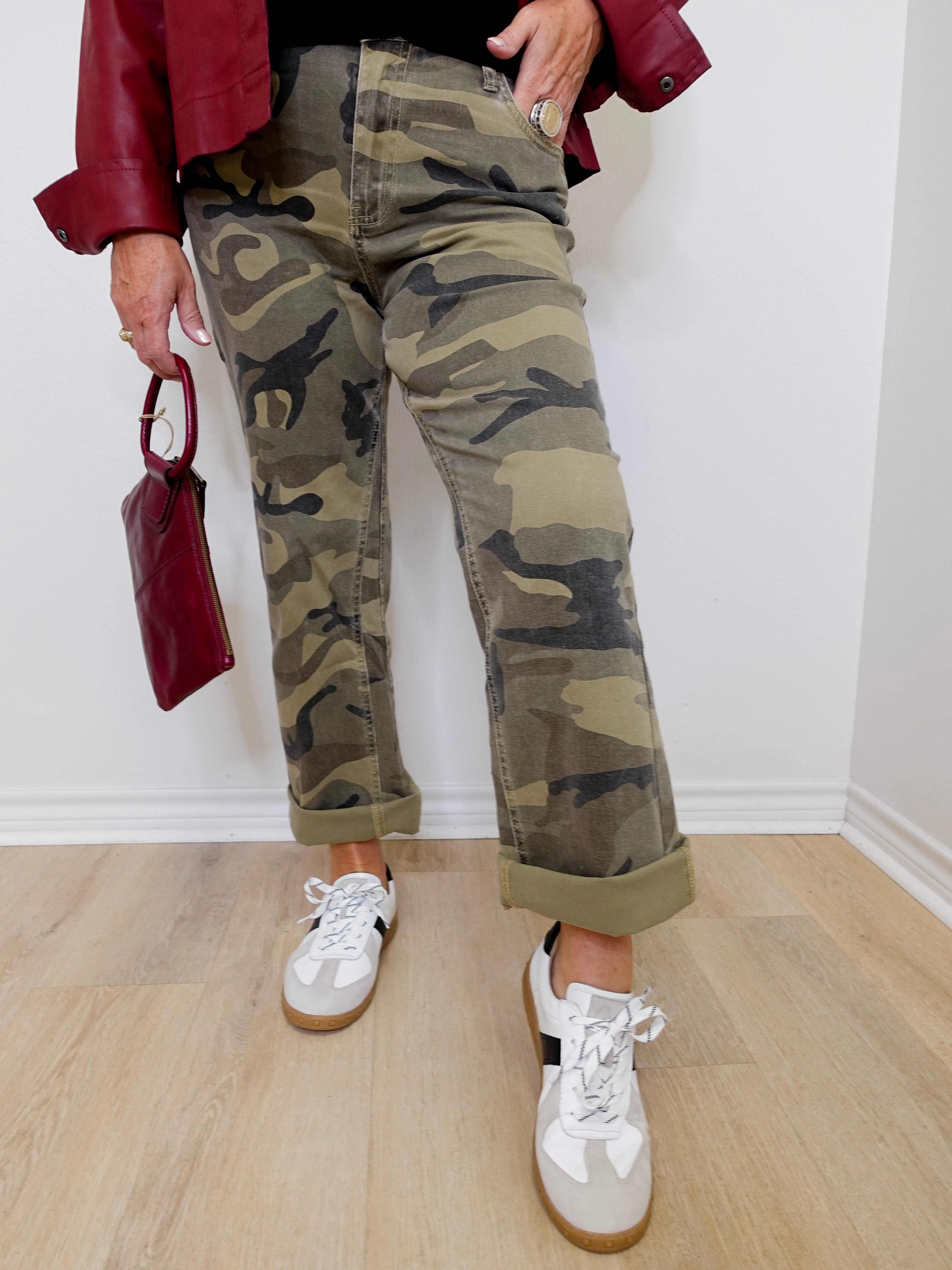 Person wearing camouflage pants and white sneakers, holding a red handbag indoors.