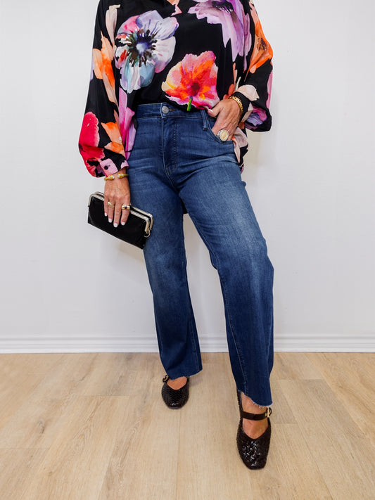 Person wearing a colorful floral blouse, blue jeans, and black shoes on a plain background