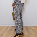 Person wearing leopard print pants and brown shoes against a white wall.