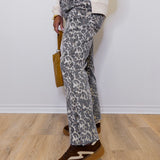 Person wearing leopard print pants and brown shoes against a white wall.