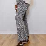 Person wearing gray leopard print pants and brown shoes on a light wooden floor.