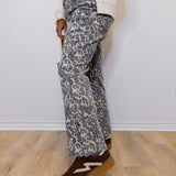 Person wearing gray leopard print pants and brown shoes on a light wooden floor.