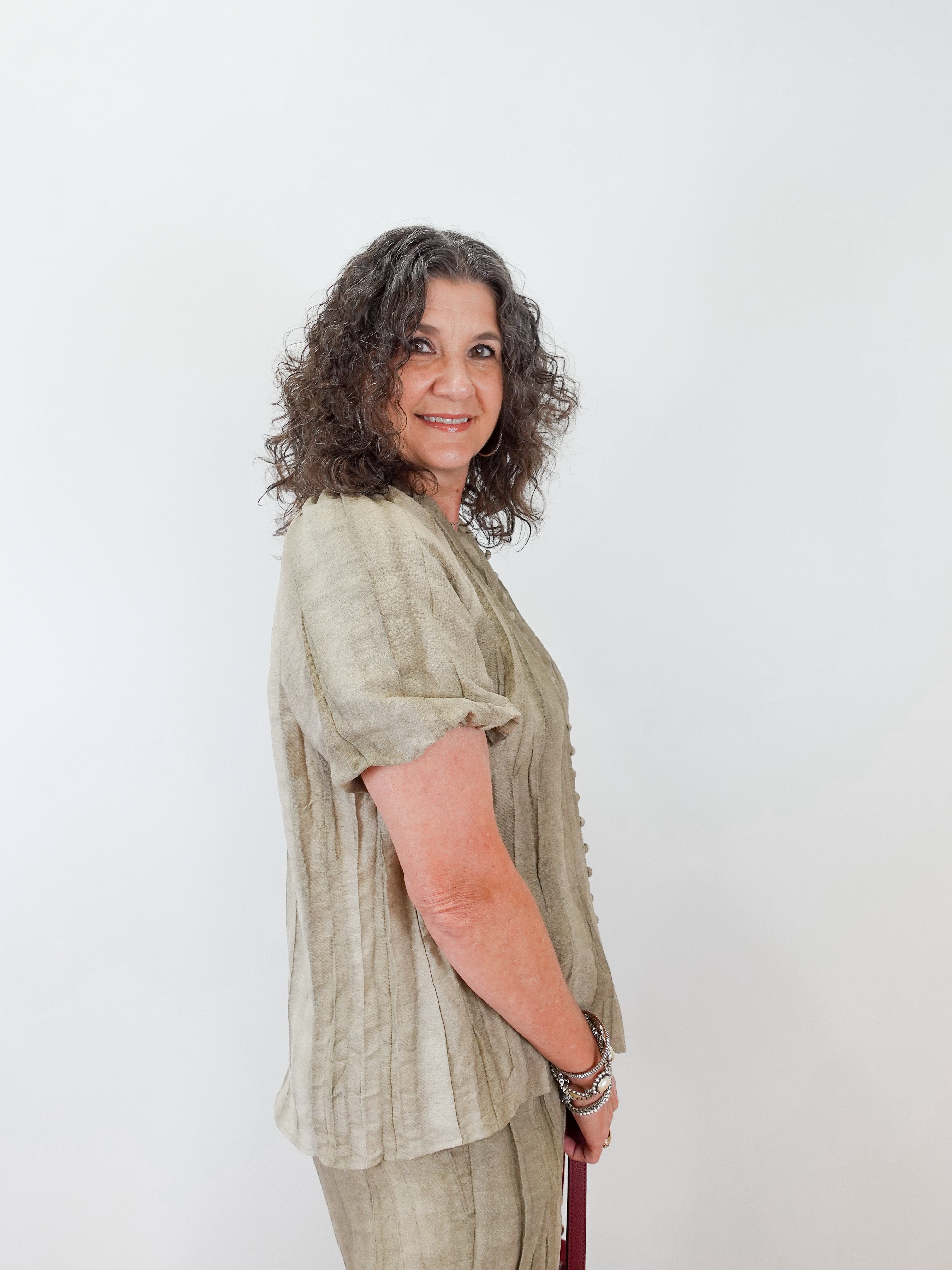 Woman wearing a light green blouse and beige pants against a white background