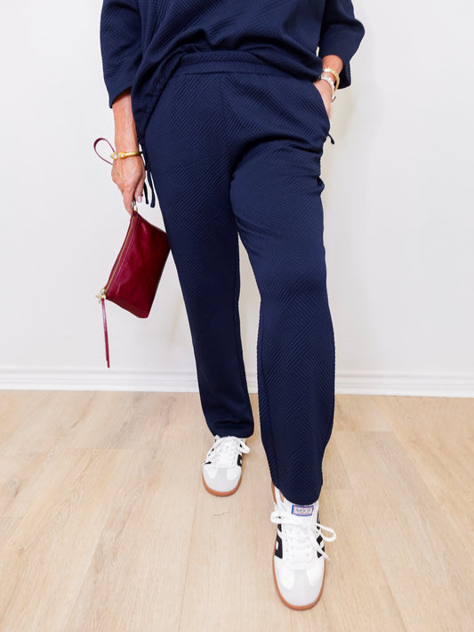 Person wearing navy tracksuit with white sneakers on a light wooden floor.