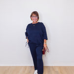 Person wearing a navy blue outfit with white sneakers against a white wall.