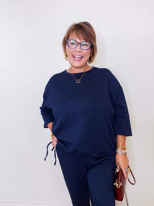 Woman wearing a navy blue outfit with glasses against a white background