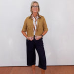 Woman wearing a brown shirt, black pants, and white shoes against a plain background