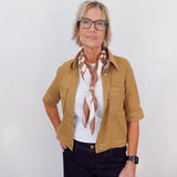 Woman wearing a tan jacket, white shirt, and black pants with a scarf against a white background