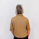 Person wearing a brown shirt and dark pants against a white background