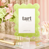 Green scalloped photo frame with 'tart by Taylor' branding on a decorative surface with flowers.