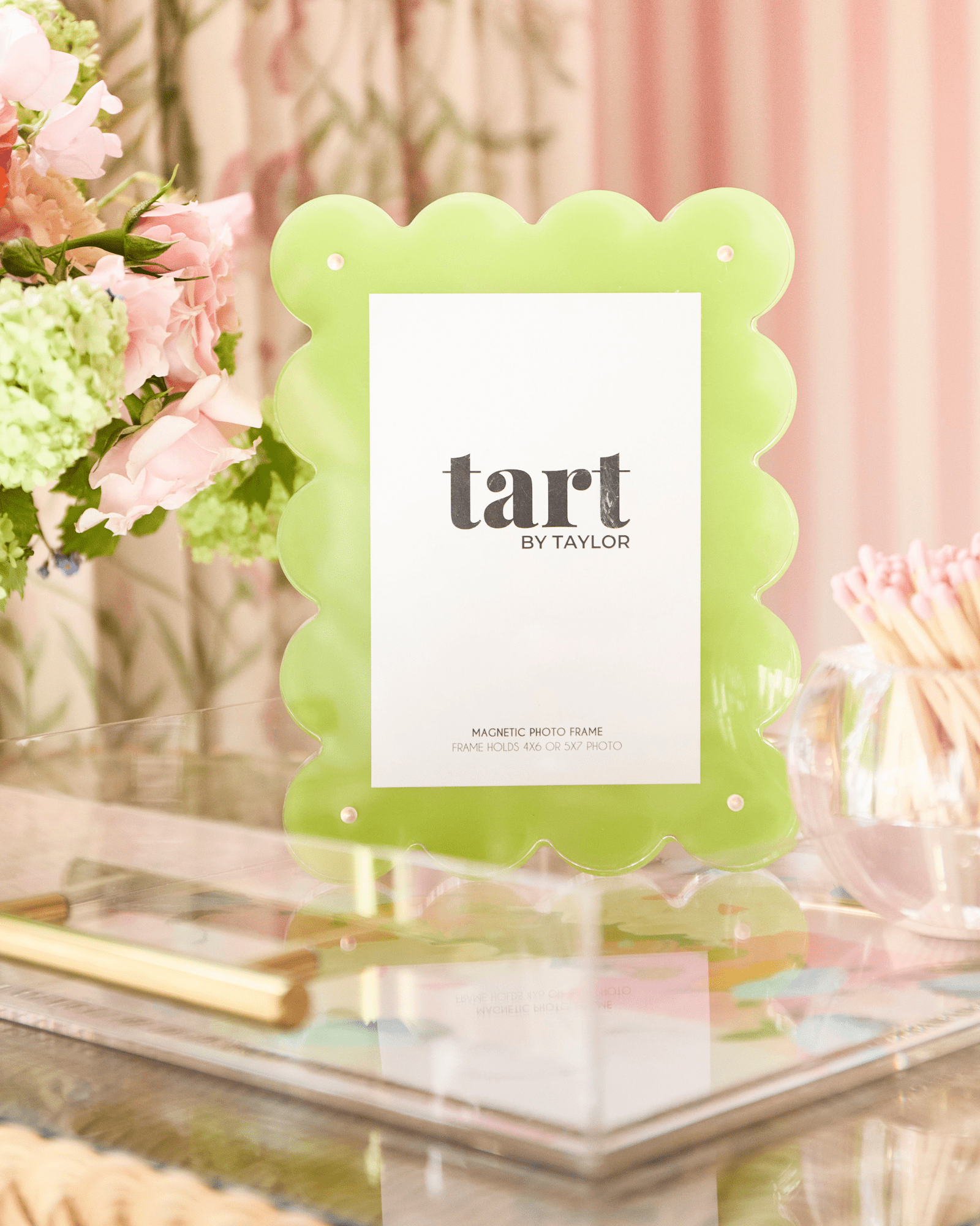Green scalloped photo frame with 'tart by Taylor' branding on a decorative surface with flowers.