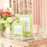 Green photo frame on a decorative table with flowers and a pink curtain in the background