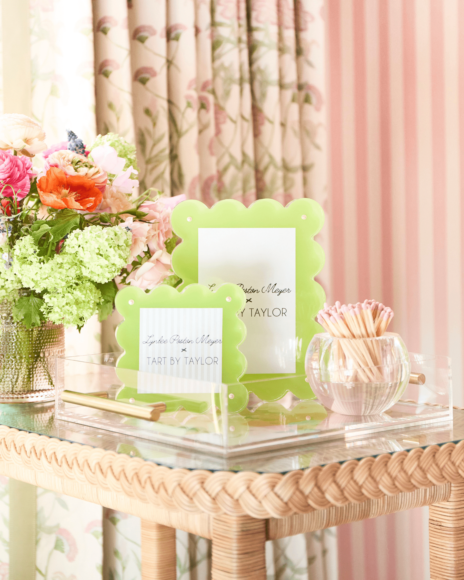Green photo frame on a decorative table with flowers and a pink curtain in the background