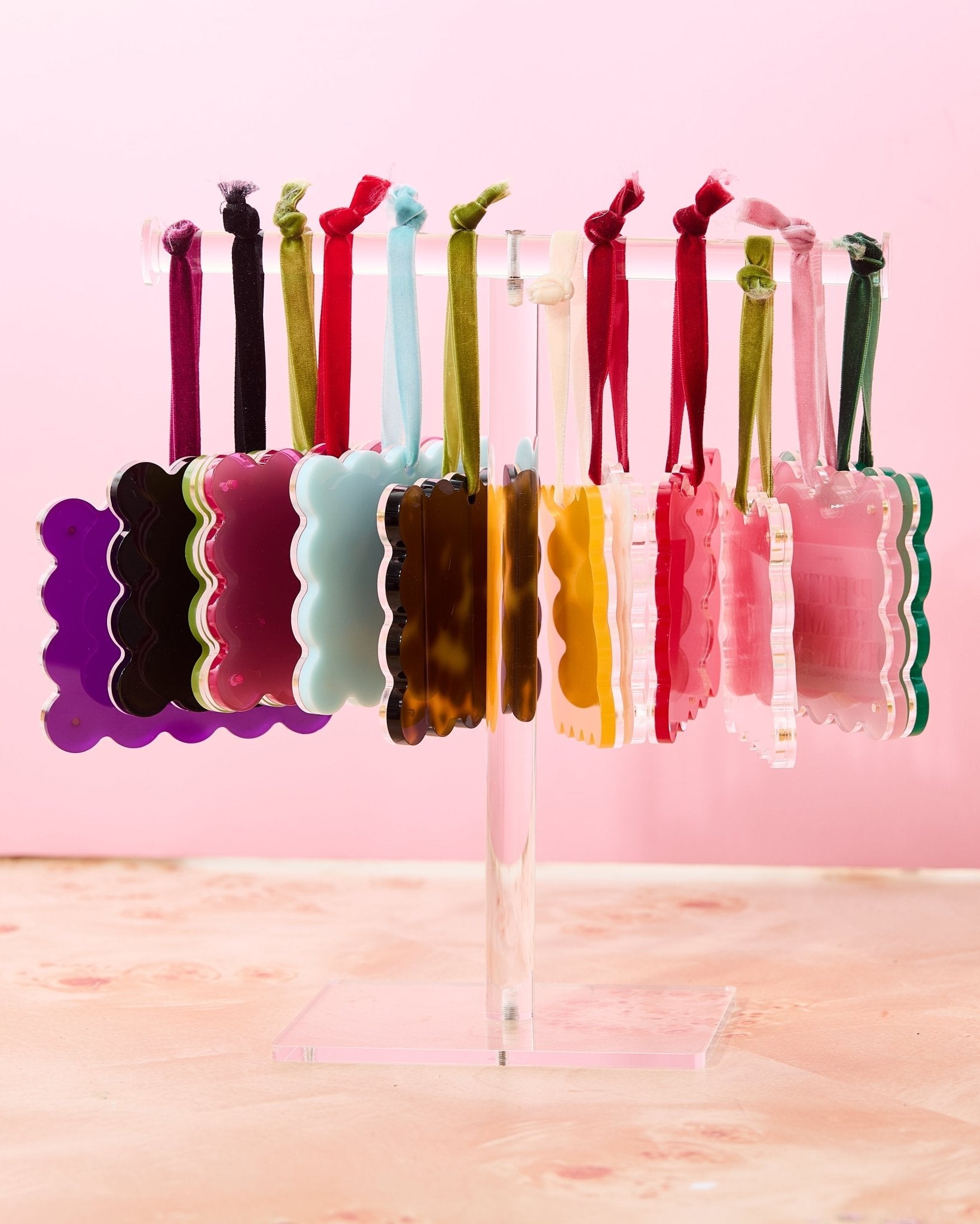 Colorful hair ties on a clear stand against a pink background