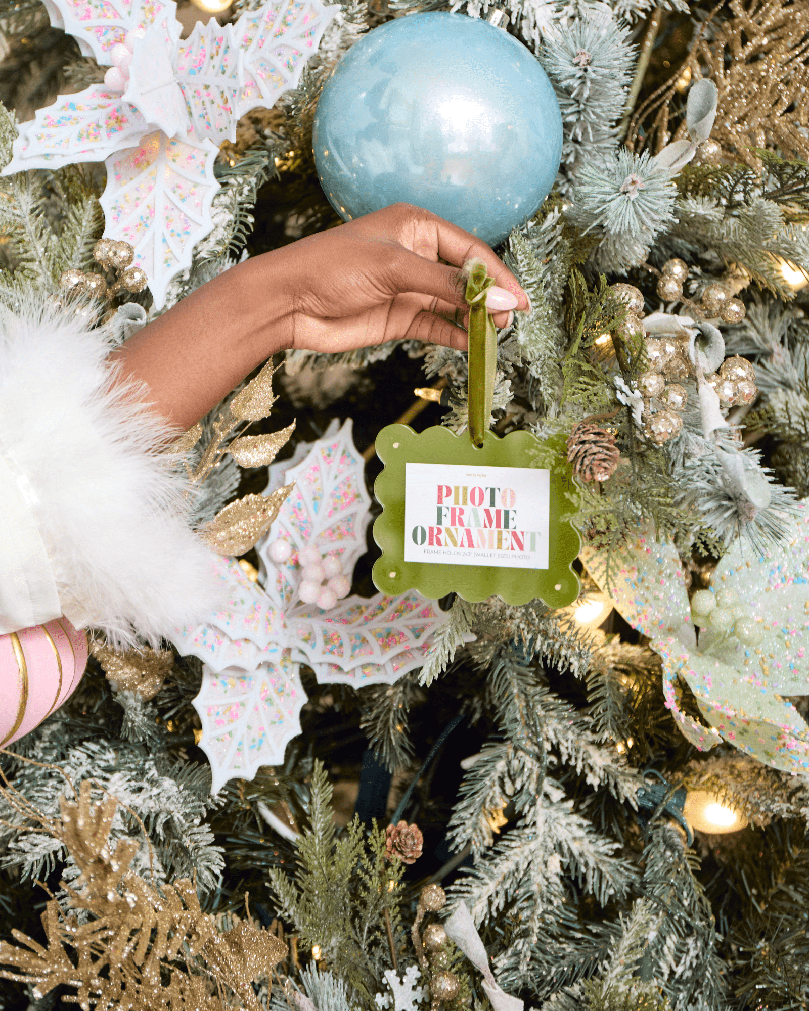 Hand holding a photo frame ornament on a decorated Christmas tree