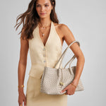 Woman holding a woven handbag against a plain background