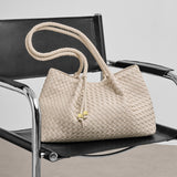 Beige woven handbag with a rope handle on a black chair.