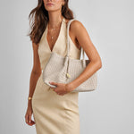 Woman holding a woven handbag against a plain background