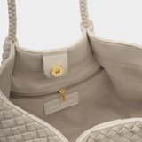 Close-up of a beige handbag with braided handles and woven pattern.