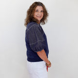 Woman wearing a navy blue top and white skirt against a plain background