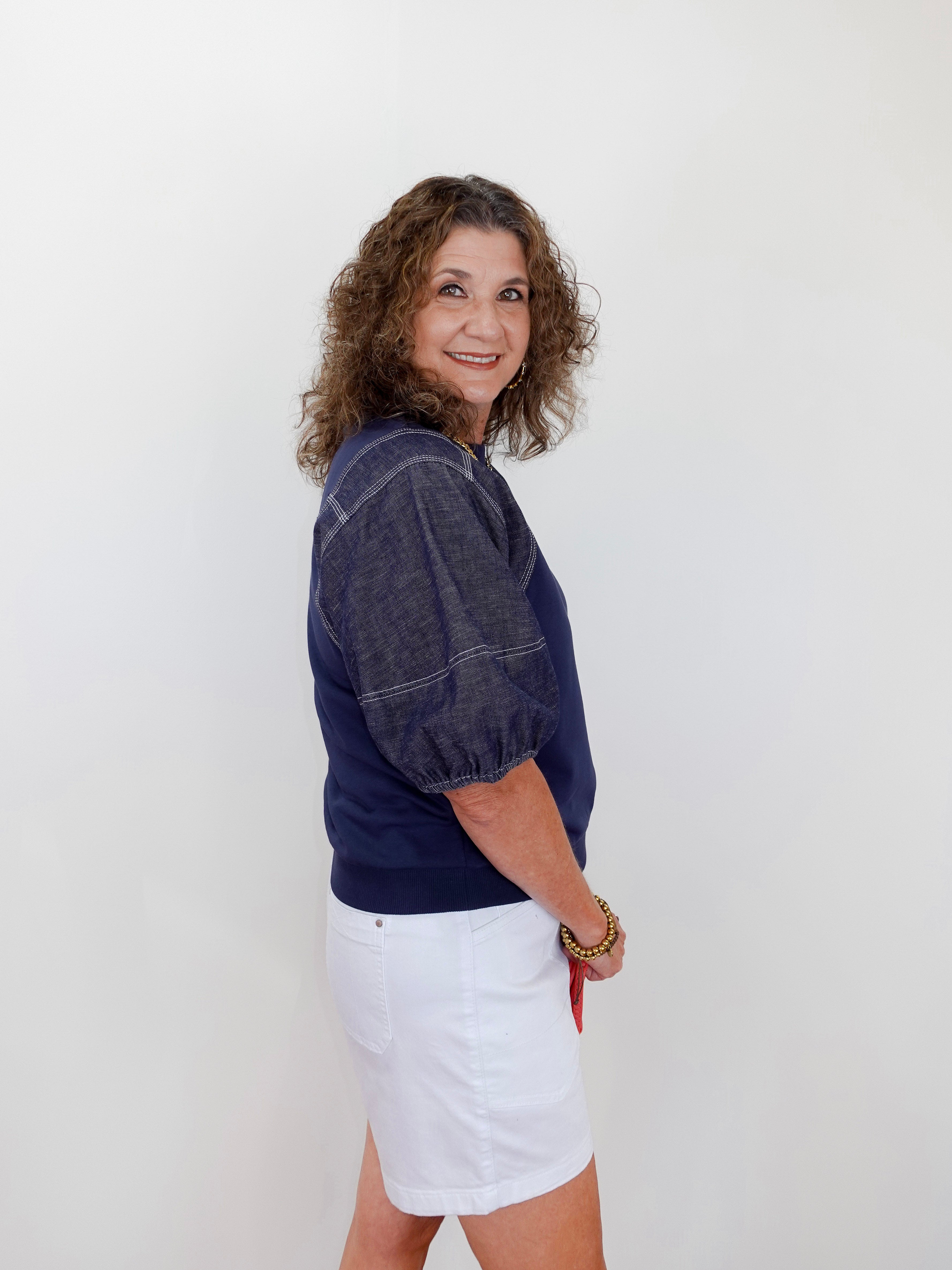 Woman wearing a navy blue top and white skirt against a plain background