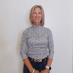 Woman wearing a patterned long-sleeve top and jeans against a plain background